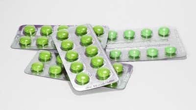 Round, green pills are shown in blister packaging.