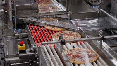 An automatic shrink wrapping machine wraps pizzas on a production line.