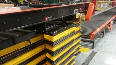 Lift tables are shown in use below a conveyor system.