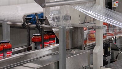 A vertical shrink wrapping machine wraps jars of pasta sauce.
