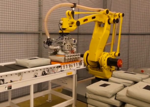 A robotic bag palletizer removes items from a conveyor and stacks them on a pallet.