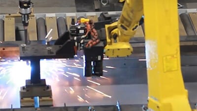 An industrial robot completes welding along a conveyor line.