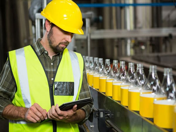 A warehouse worker checks bottles on a liquid fill line.