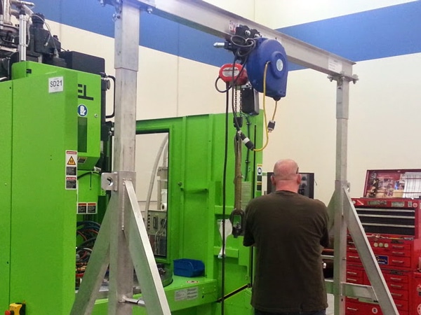 A man works next to a gantry crane in a warehouse.