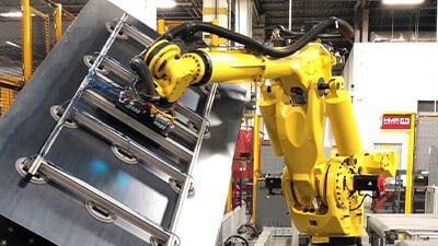 An industrial robot uses end-of-arm-tooling to lift a piece of metal.